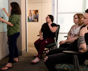 PhD students discuss their work as one student writes on a whiteboard.